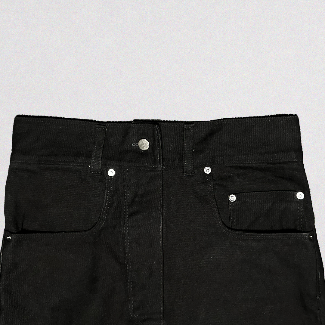 Close-up of the waistband and front pockets of black denim jeans with silver metal rivets and a silver button, set against a plain light gray background.