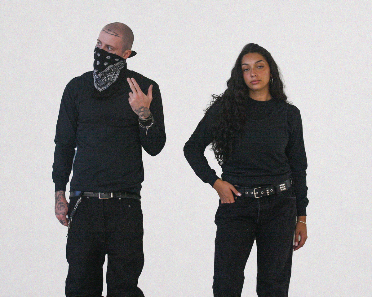 Two models posing in matching black streetwear outfits, including long-sleeve shirts, black jeans, and black belts, against a plain white studio background.