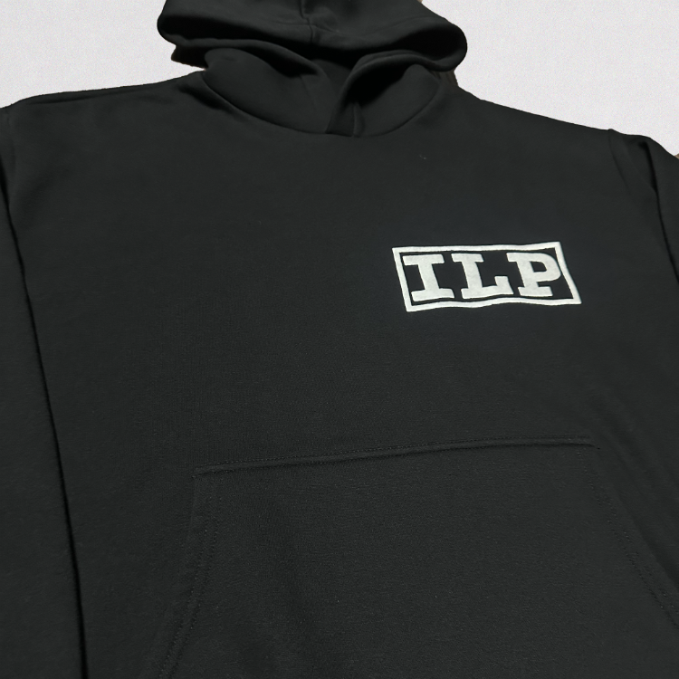 A close-up of a black pullover hoodie featuring a white outlined 'ILP' logo on the left chest, set against a light gray background.