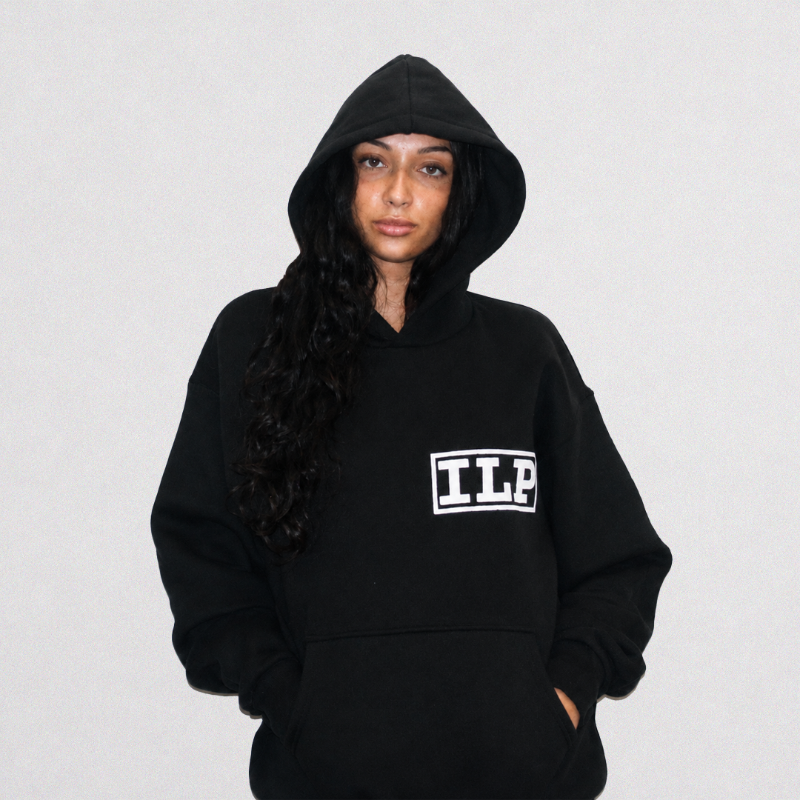 A woman wearing a black pullover hoodie with a white block-letter 'ILP' logo on the left chest, posed against a plain white studio background.