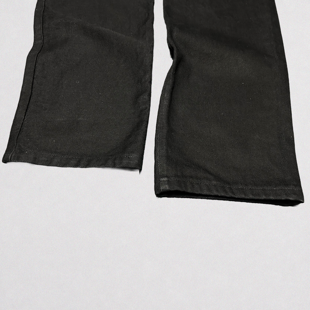 Close-up of the lower legs of black denim pants laid flat on a light gray background.