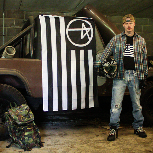 Model in denim standing beside a jeep with the black and white striped ilovepunx pentagram flag, 2025